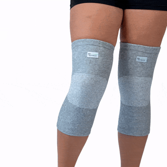 Close-up of a person wearing a pair of light grey bamboo knee compression sleeves. The sleeves feature a visible ribbed compression band over the knee joint and a small bamboo fabric label.