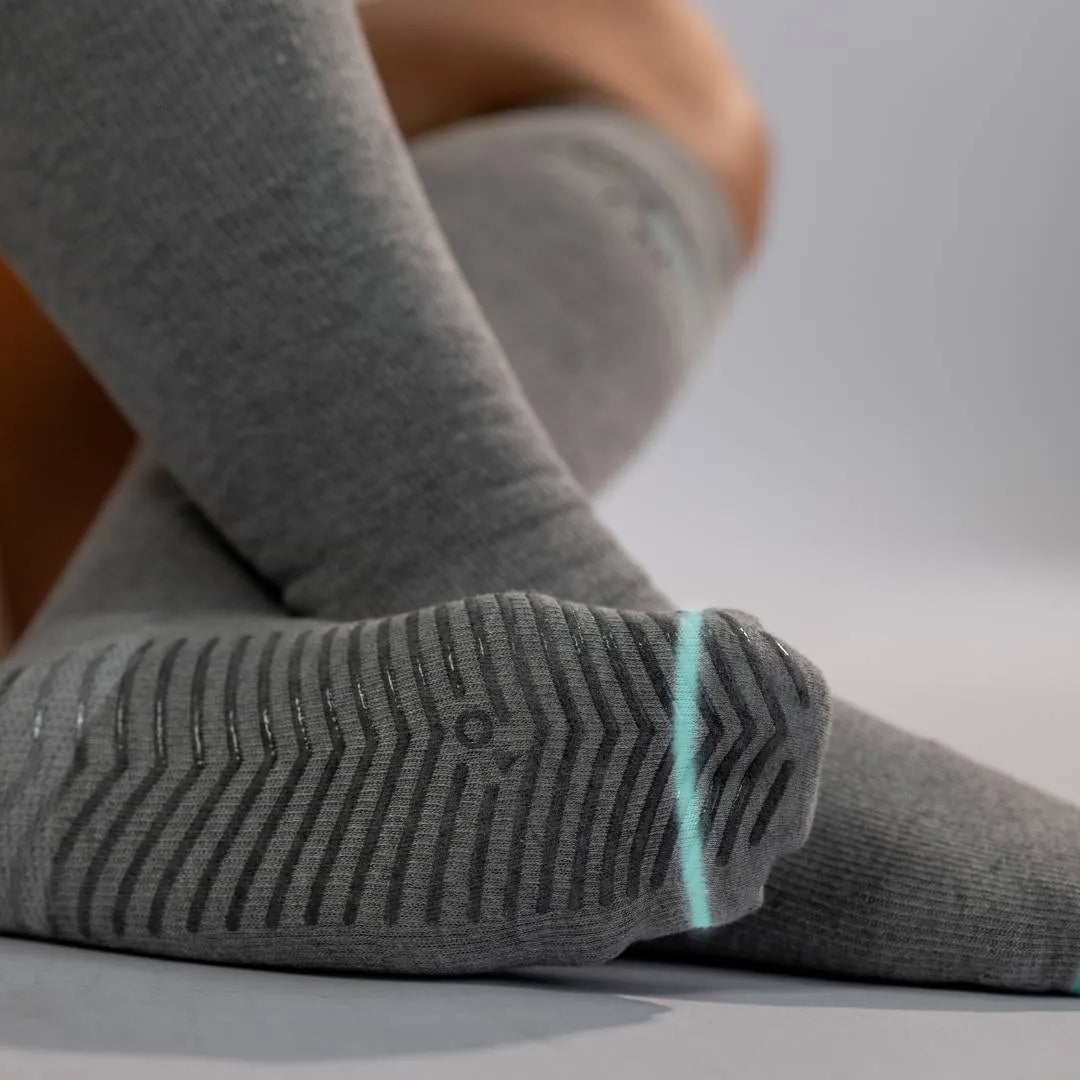 Close-up view of the non-slip grip sole on grey compression socks featuring a chevron pattern of silicone tread for stability and safety.